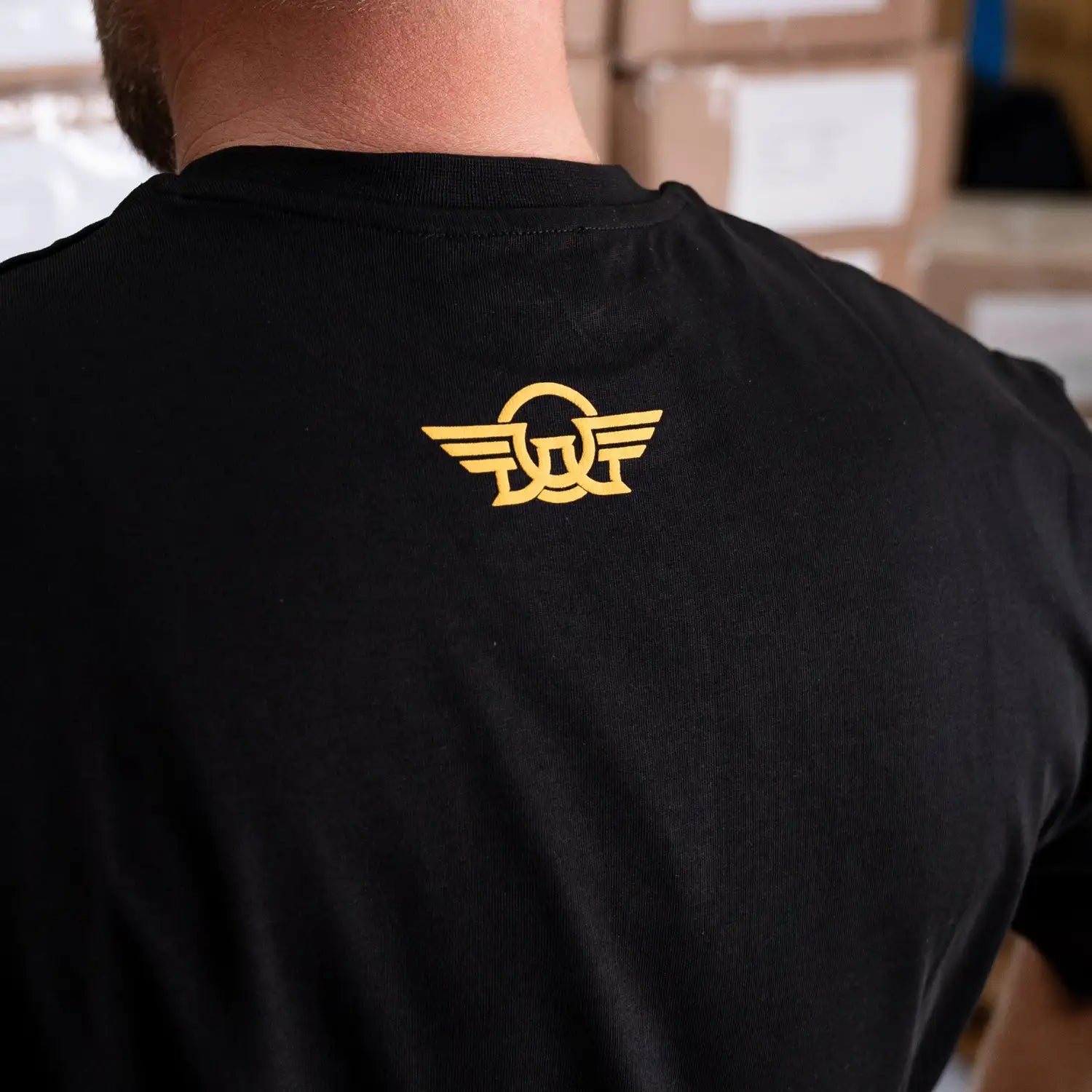 Rückansicht: schwarzes Oversize T-Shirt mit kleinem gelben DAG-Logo im Nacken