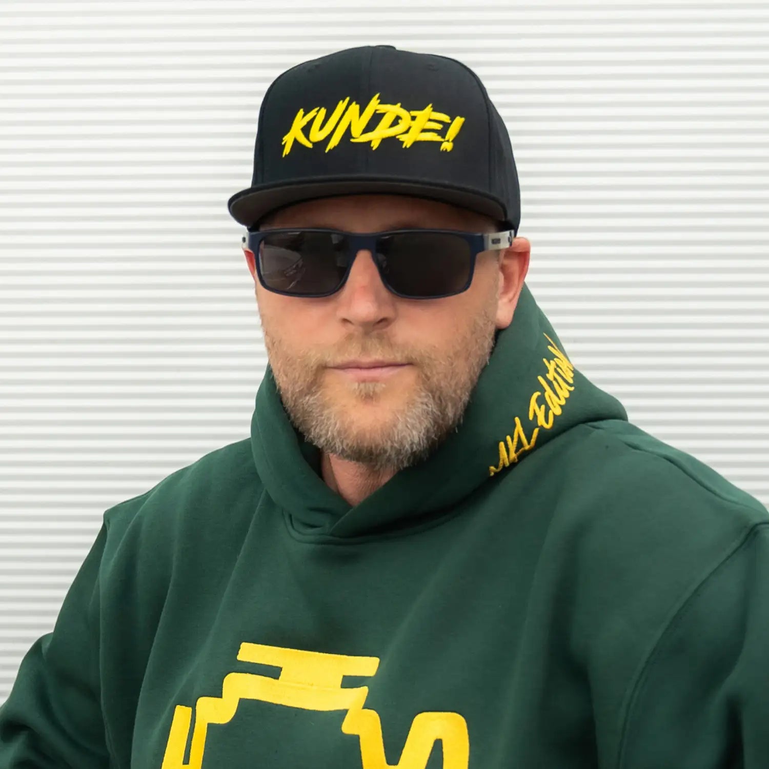 Schwarze KUNDE! Cap mit gelbem Stick seitlich am Kopf getragen, sichtbare Passform und Form der Kappe.