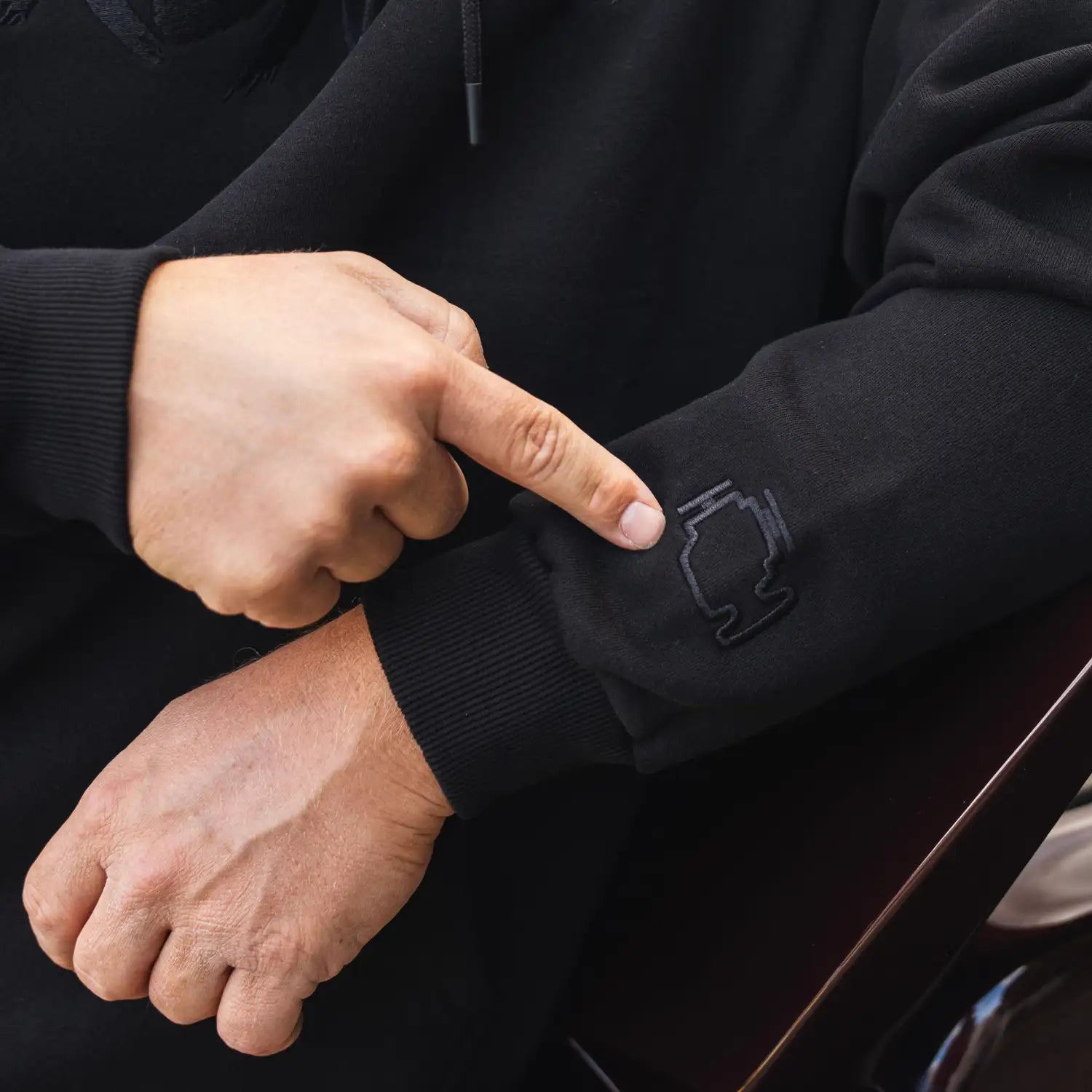 Detailaufnahme des Ärmel-Sticks am Kunde Hoodie in Schwarz/Anthrazit mit gesticktem DAG-Logo.