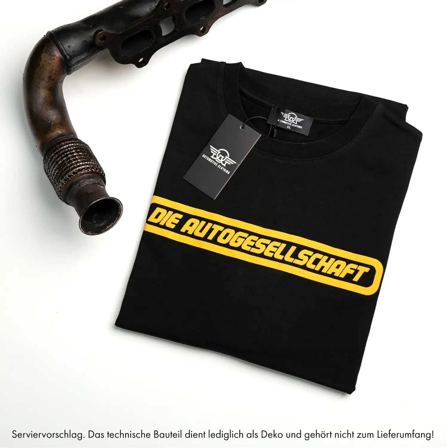 Gefaltetes schwarzes Oversize T-Shirt mit gelbem Frontschriftzug neben Auspuffteil – Automotive-Style