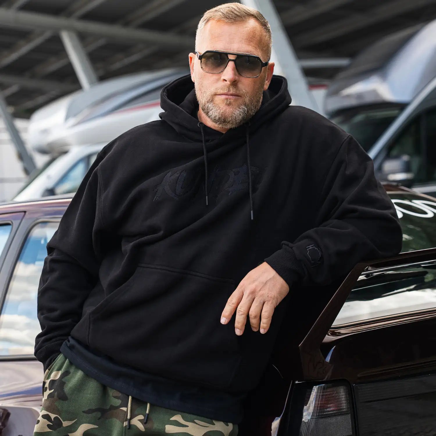 Kunde Hoodie in Schwarz/Anthrazit, Gesamtansicht von vorne. Oversized Passform mit gesticktem Brustlogo.